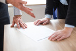 Unrecognizable business people discussing document. One person gesturing, other leaning on table. Business paper on desk. Teamwork concept